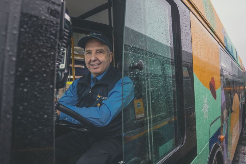Bus operator smiling behind wheel of bus .