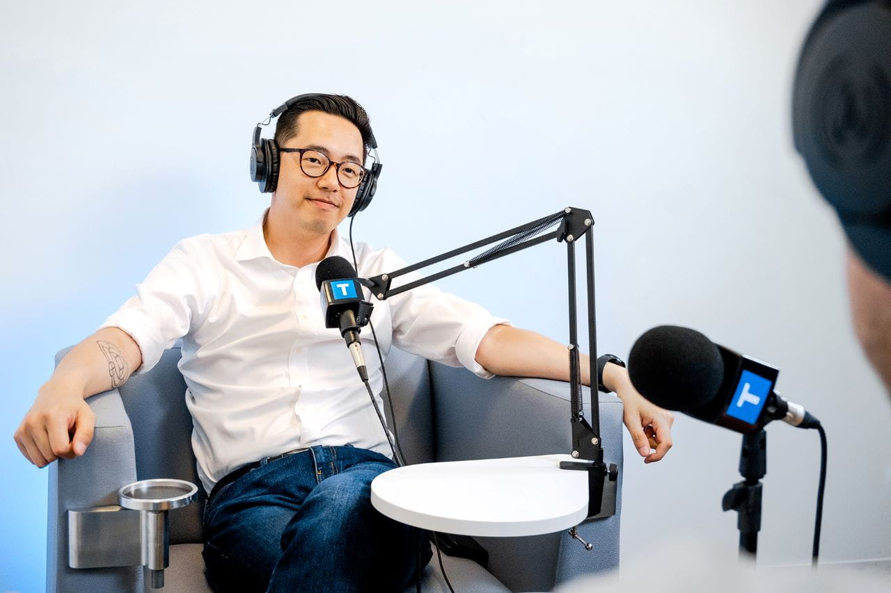 Photo of podcast host Jawn Jang sitting in a chair. Jawn has headphones and is listening to a guest speak during an interview. 