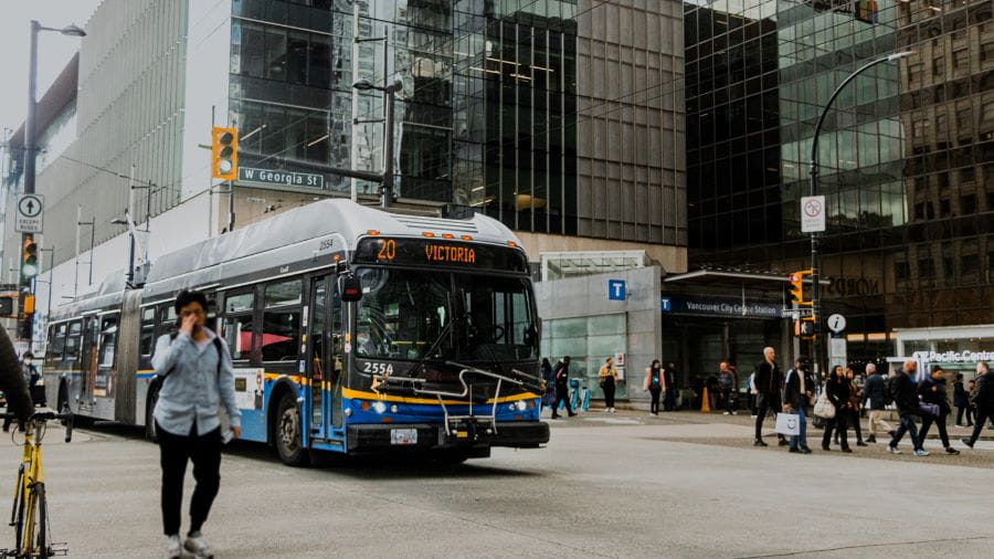 Entrance to Vancouver City Centre Canada Line station in downtown Vancouver with bus, high-rise, and people walking.