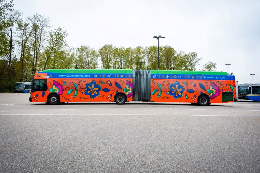 Articulated bus parked at transit centre with colourful Vaisakhi-themed wrap on bus