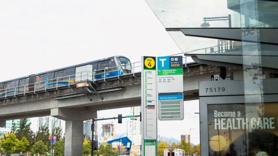View of SkyTrain on elevated guideway at King George Station with bus stop and bus shelter in foreground.