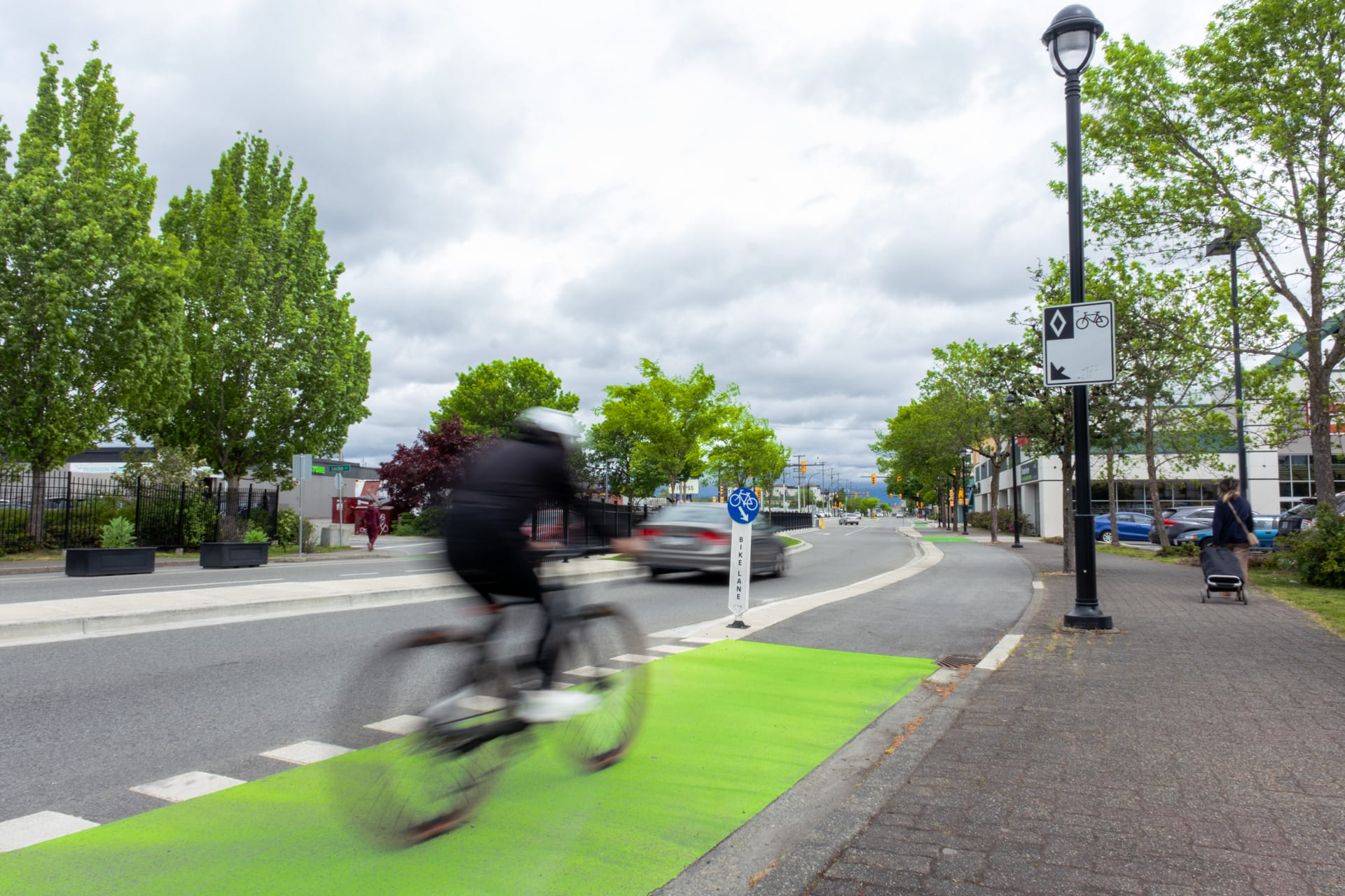 A cyclist rides their bike down a designated bike path while a car is driving past them in the adjacent lane
