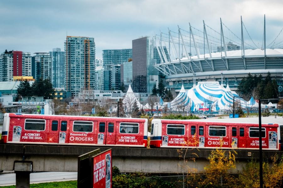 Wrapped SkyTrain passing by Taylor Swift billboard with BC Place in the background