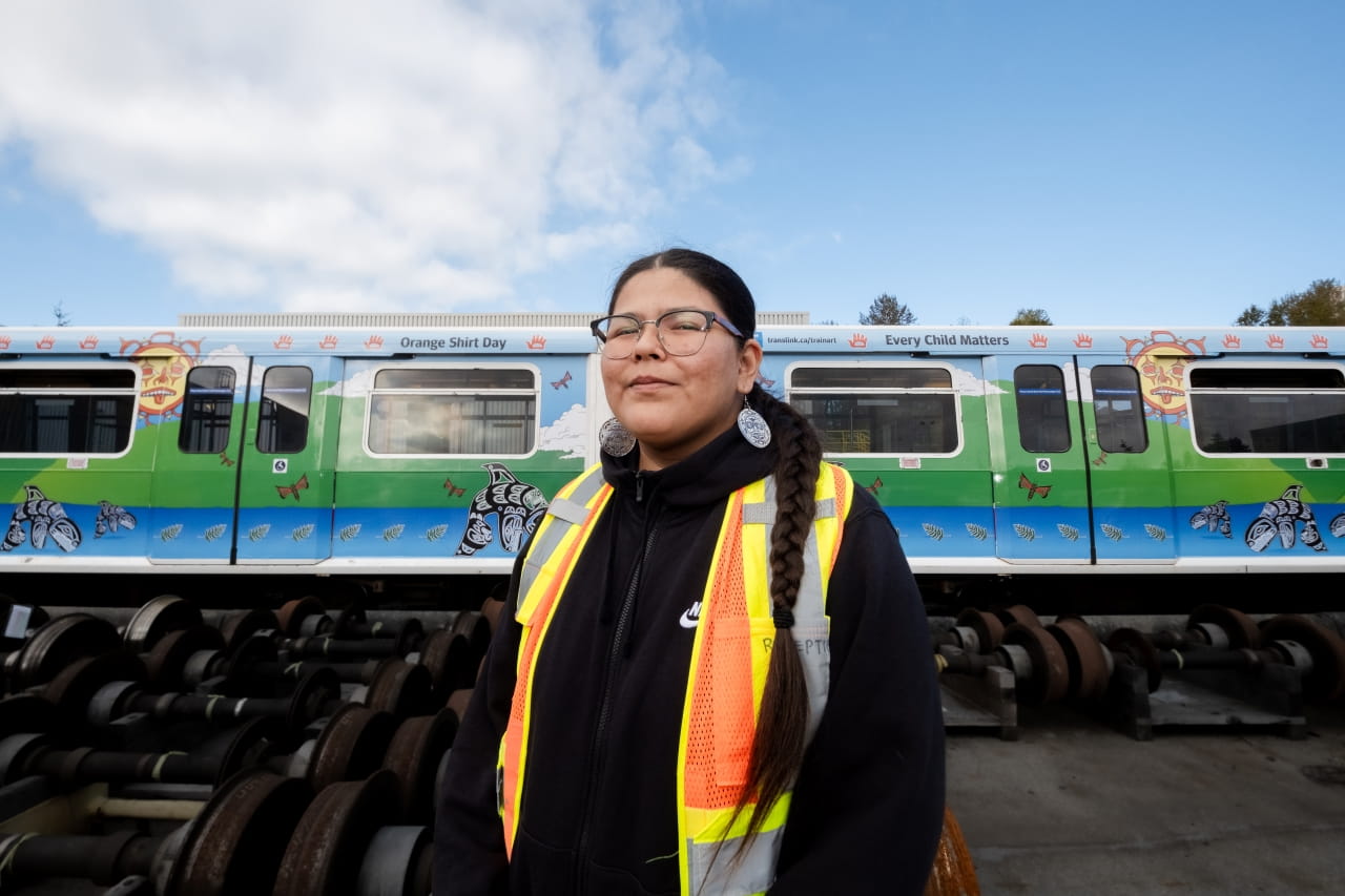 Shonta Campbell (Kishiqweb), a Heiltsuk, Anishinaabe, and Wuikinuxv artist, standing in front of the decorated SkyTrain cars