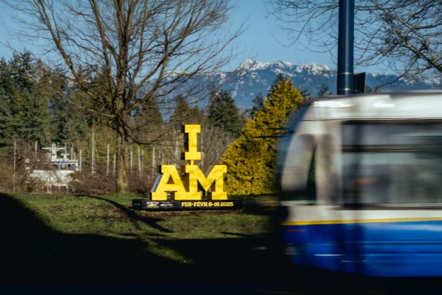 Bus passing by Invictus Games sign with trees and mountains in background