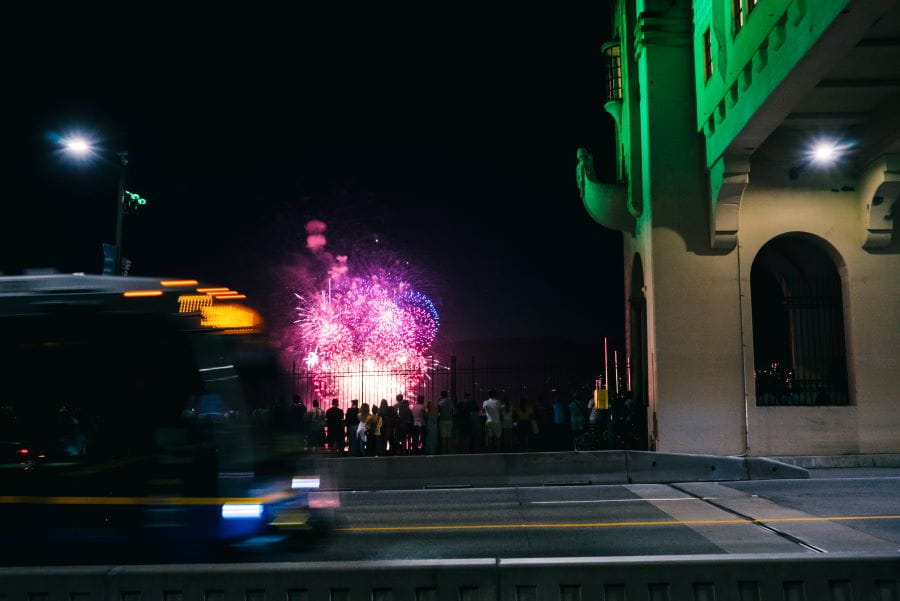 Bus driving over Burrard Street Bridge at night past pedestrians watching fireworks