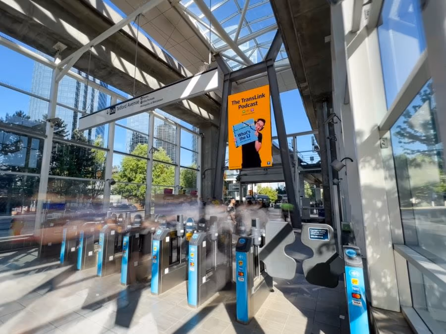 Fare gates at Metrotown Station with digital ad for TransLink podcast