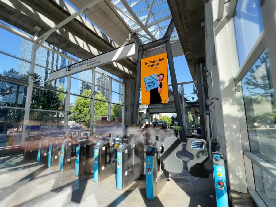 Fare gates at Metrotown Station with digital ad for TransLink podcast
