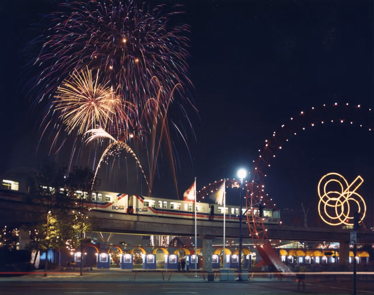 Mark I SkyTrain is running in the background while fireworks are decorating the night sky for Expo 86