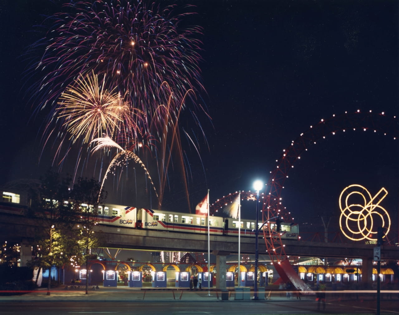 Mark I SkyTrain is running in the background while fireworks are decorating the night sky for Expo 86