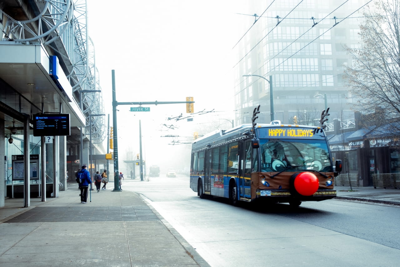 the reindeer bus is driving down a wintery street, decorated with reindeer antlers, a red nose, and eyes