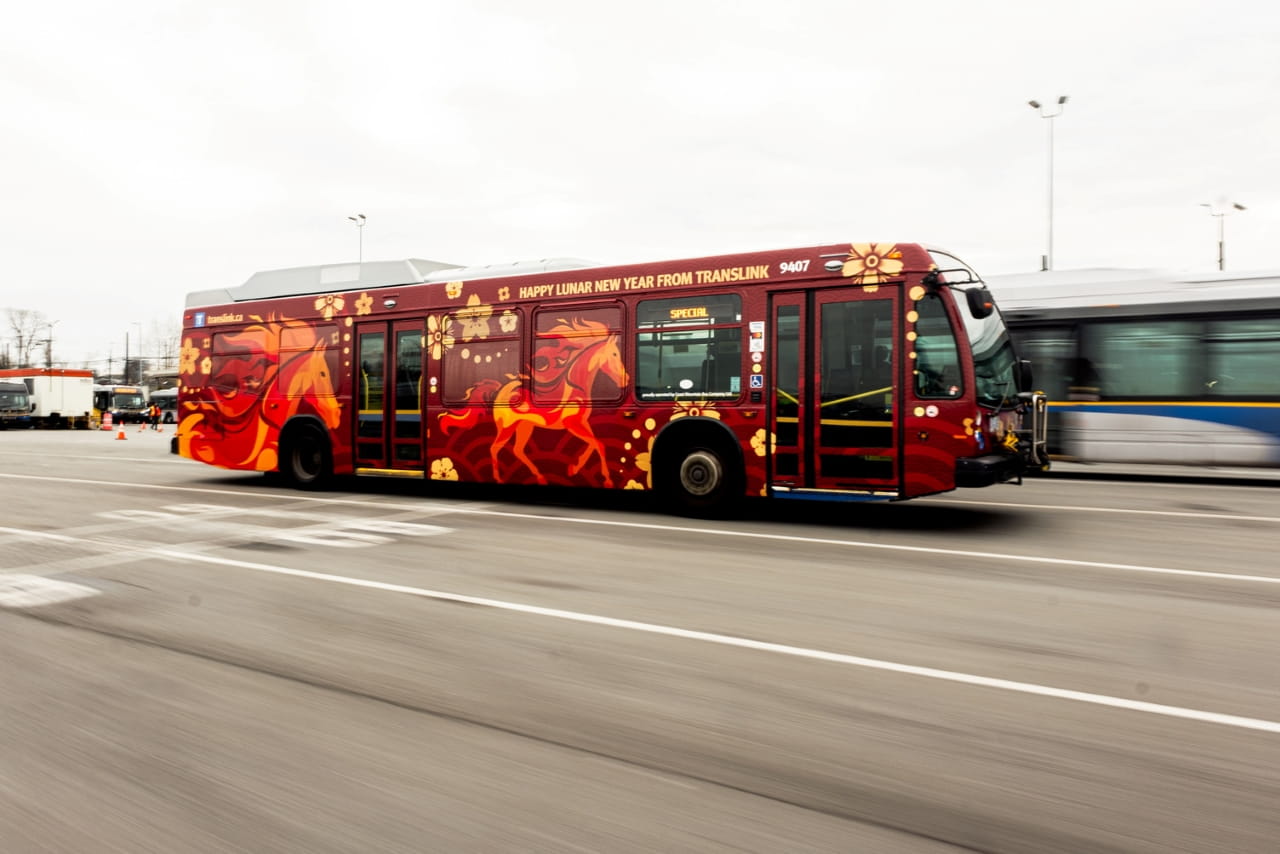 TransLink's Lunar New Year bus in motion, beautifully decorated in red and gold with orange fiery horses, representing the Year of the Horse, adorned on the sides