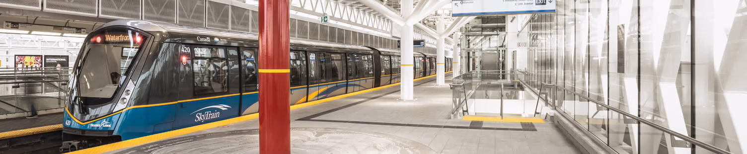 A SkyTrain docked at a station with a public art piece next to the train
